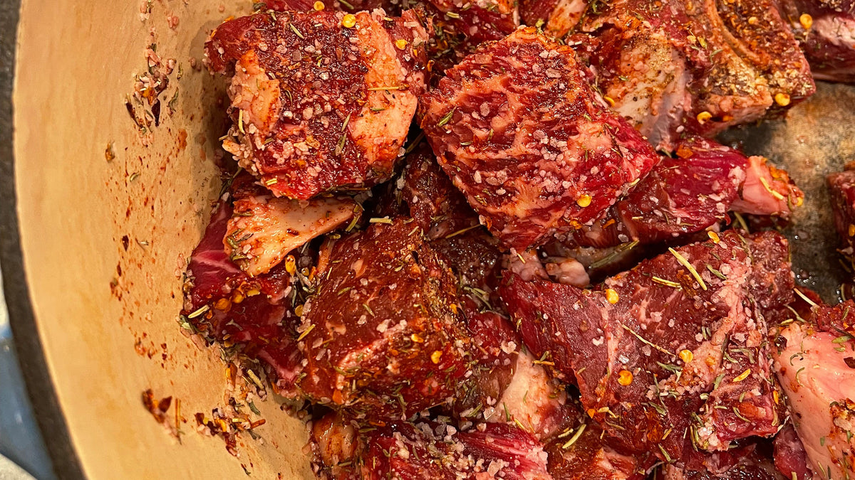 Raw beef chunks in a ceramic pot with herbs.